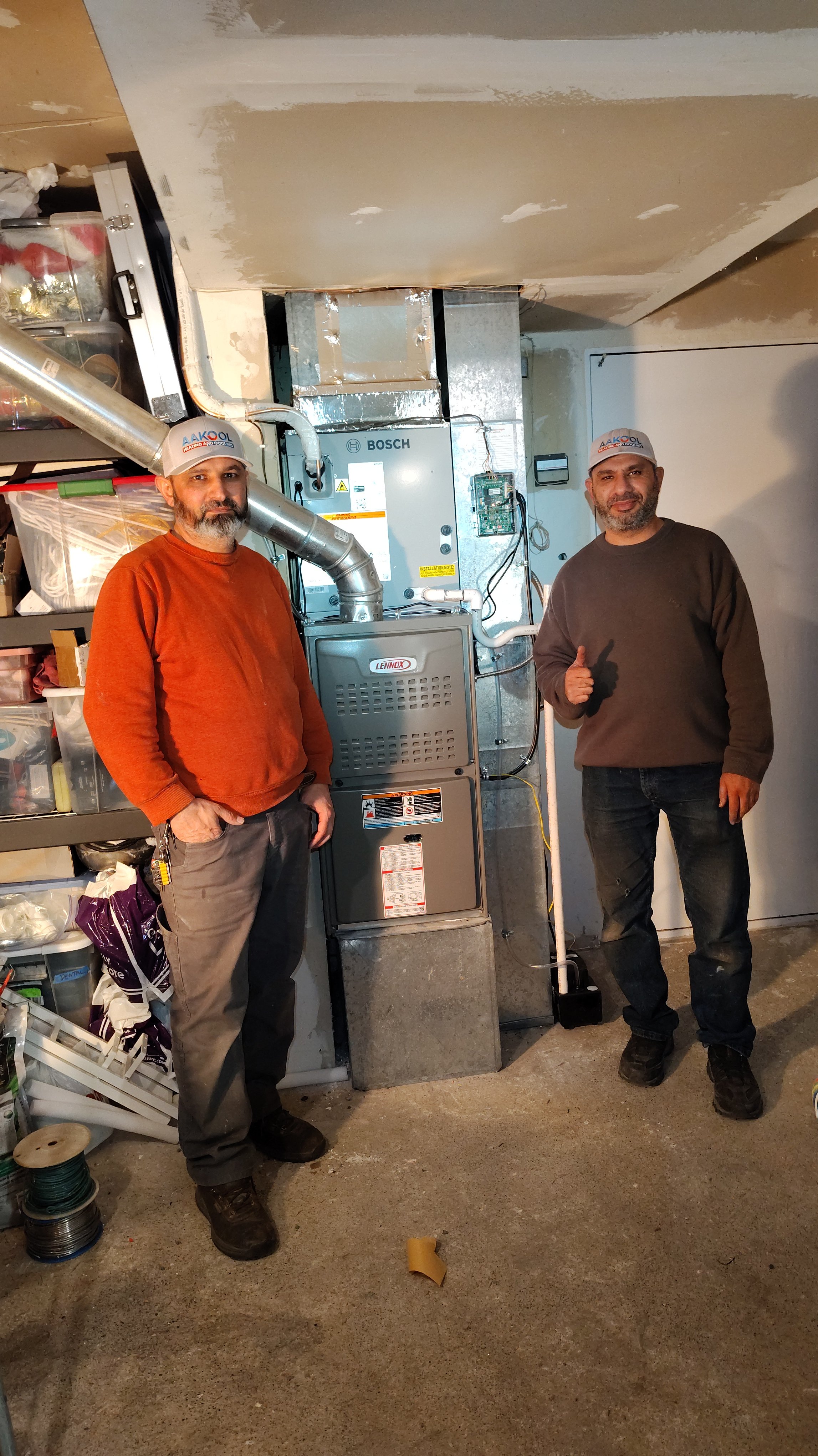Two workers pose next to a Bosch furnace in an unfinished basement renovation.