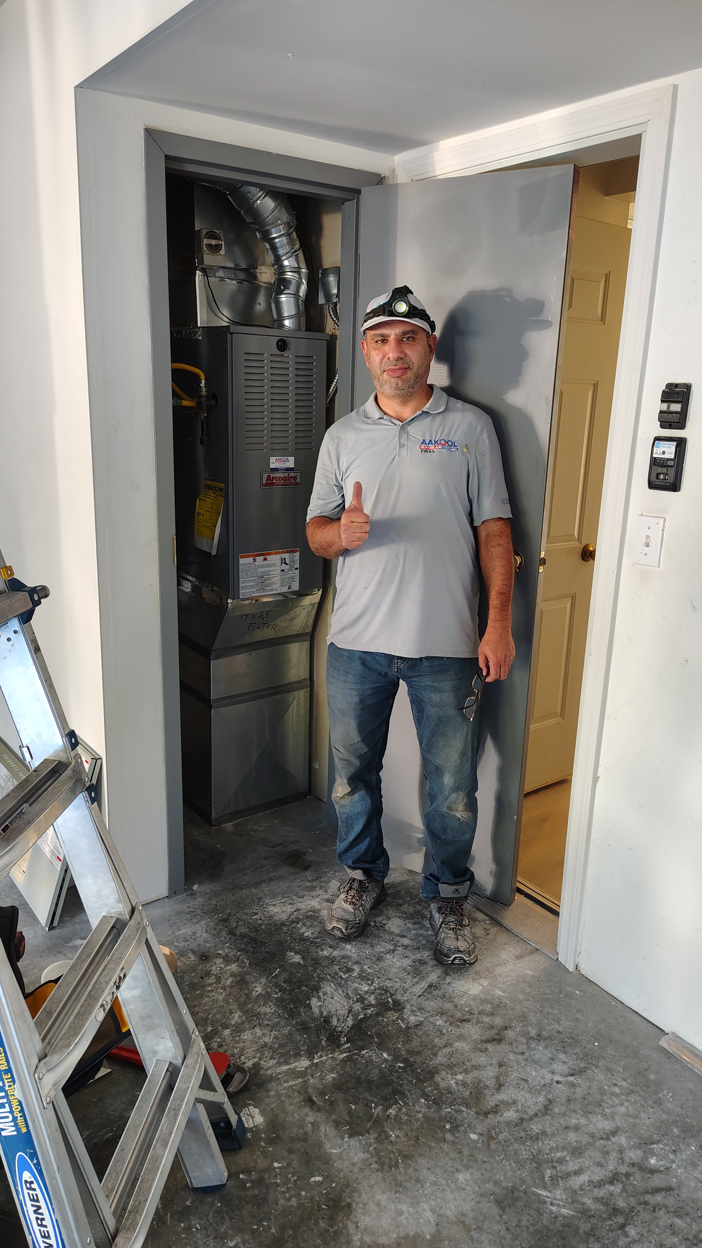 HVAC technician gives thumbs up beside furnace unit installation in garage.