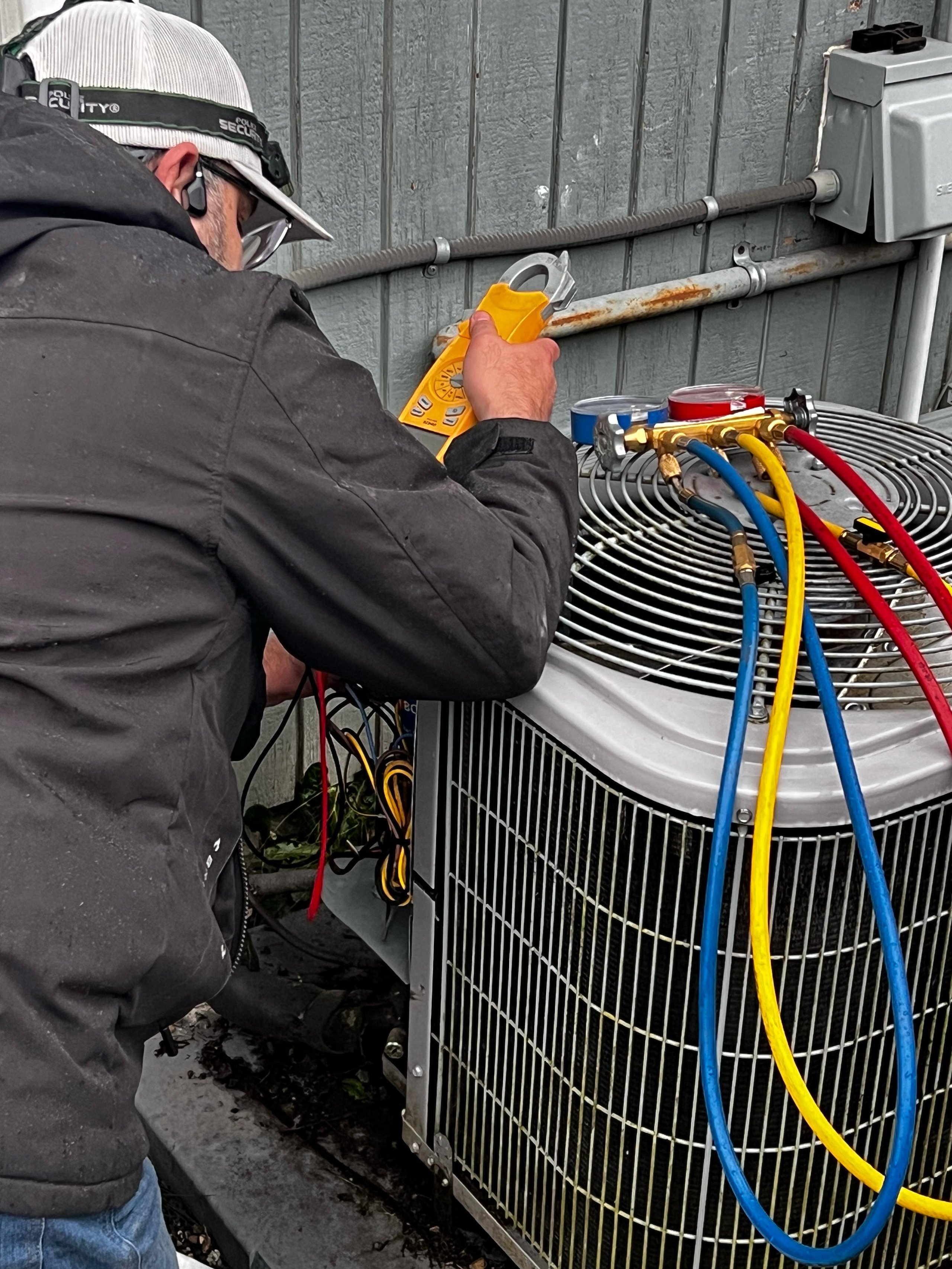 HVAC technician working on outdoor air conditioning unit with colored service hoses