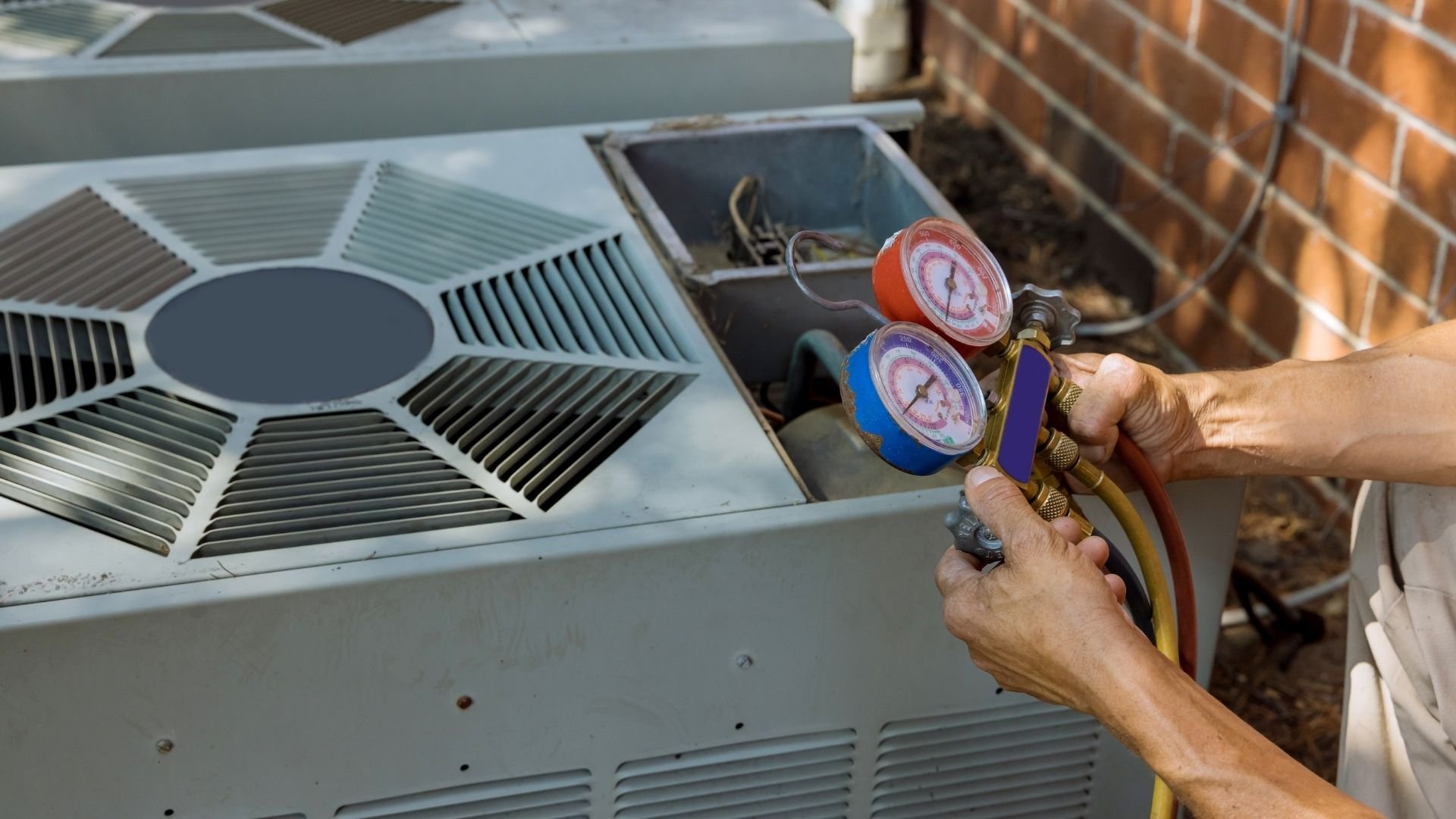 Technician holding pressure gauges on air conditioning unit for maintenance check