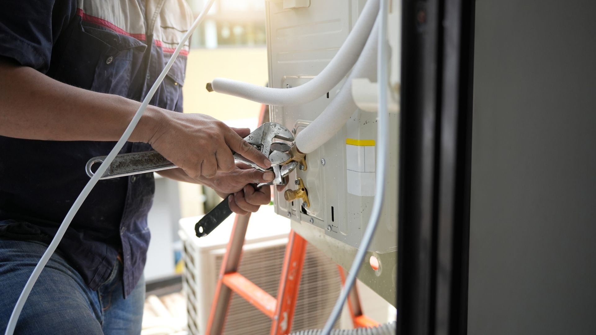 Technician installing HVAC ductwork, connecting white pipe to wall unit with wrench