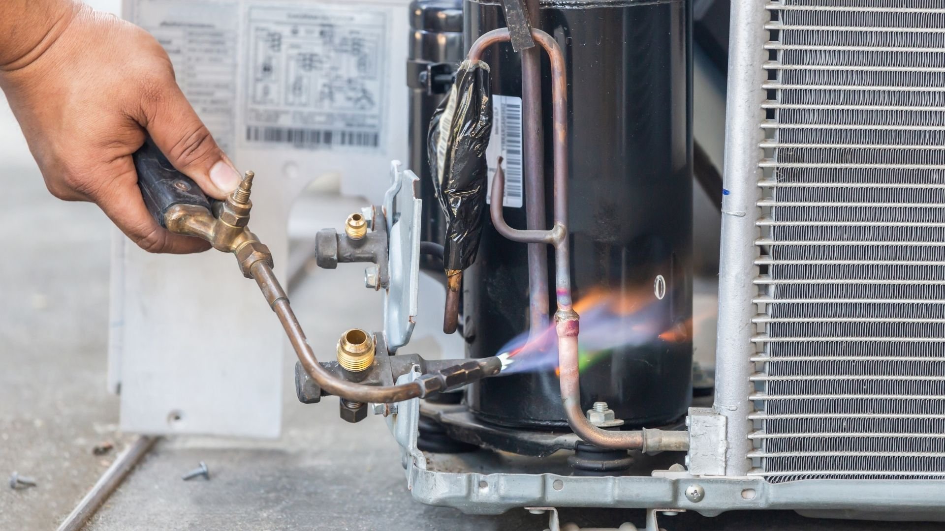 Technician holding copper tubing with blue flame testing HVAC air conditioning unit components.