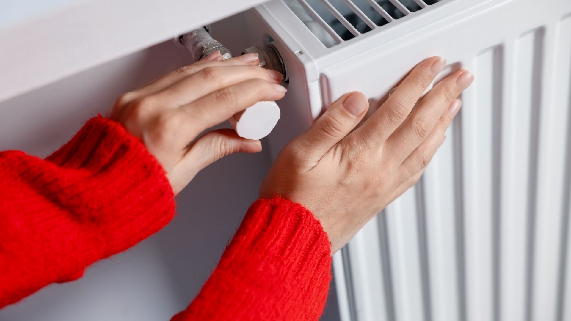 Person in red sweater adjusting temperature on white radiator thermostat