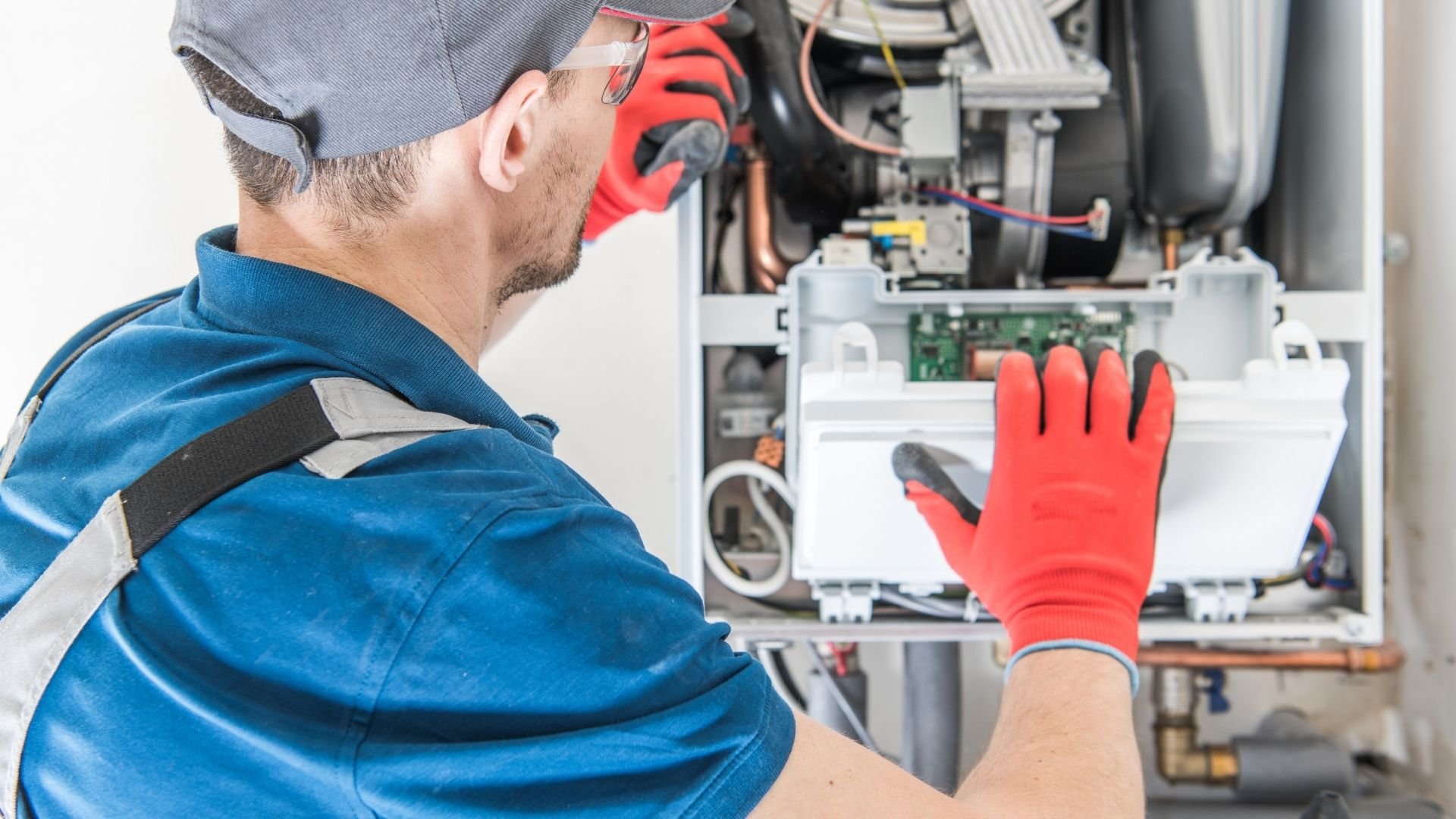 Technician in red safety gloves inspecting internal components of electronic heating equipment