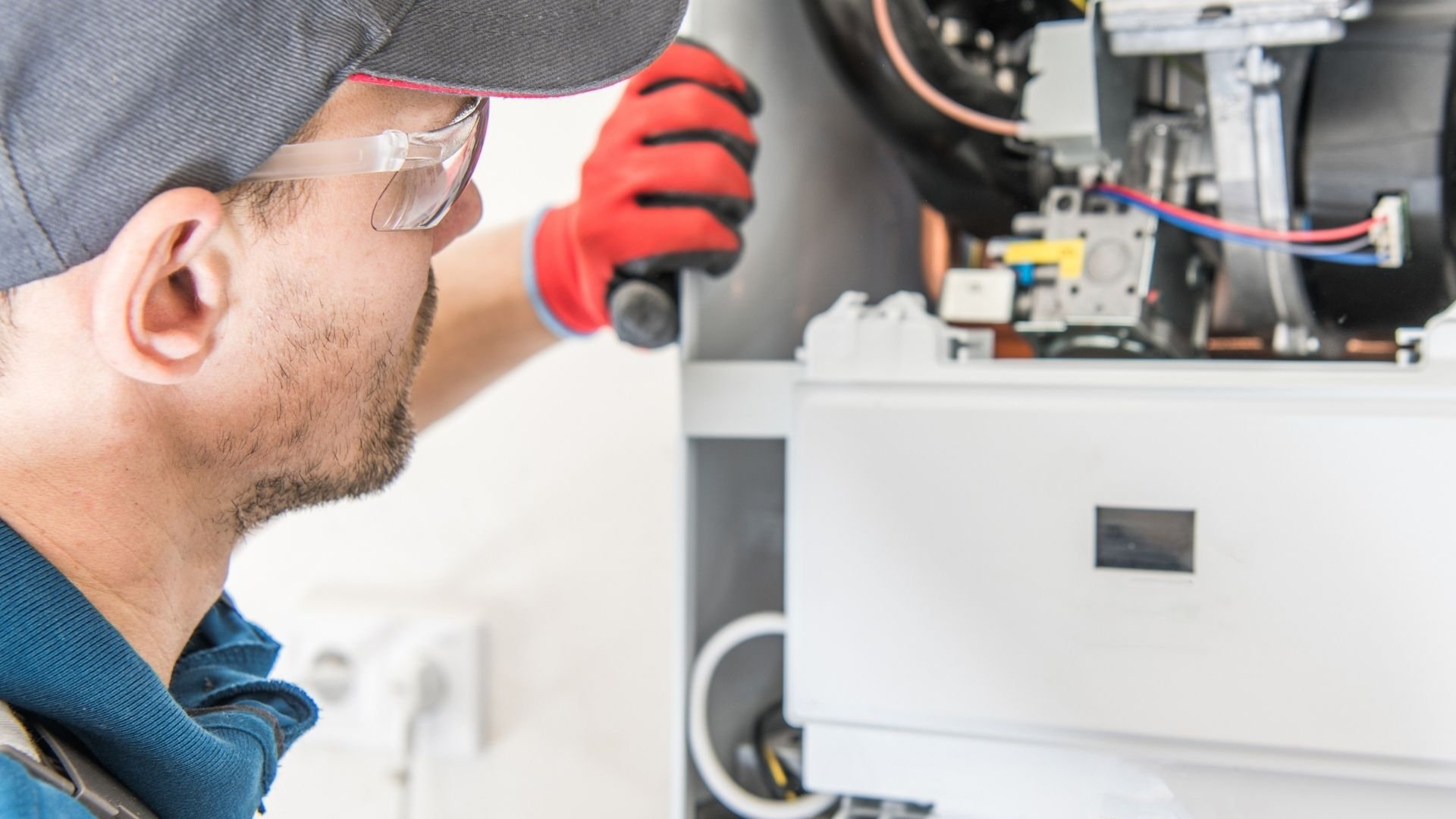 Technician wearing safety glasses and red gloves inspects electrical equipment interior