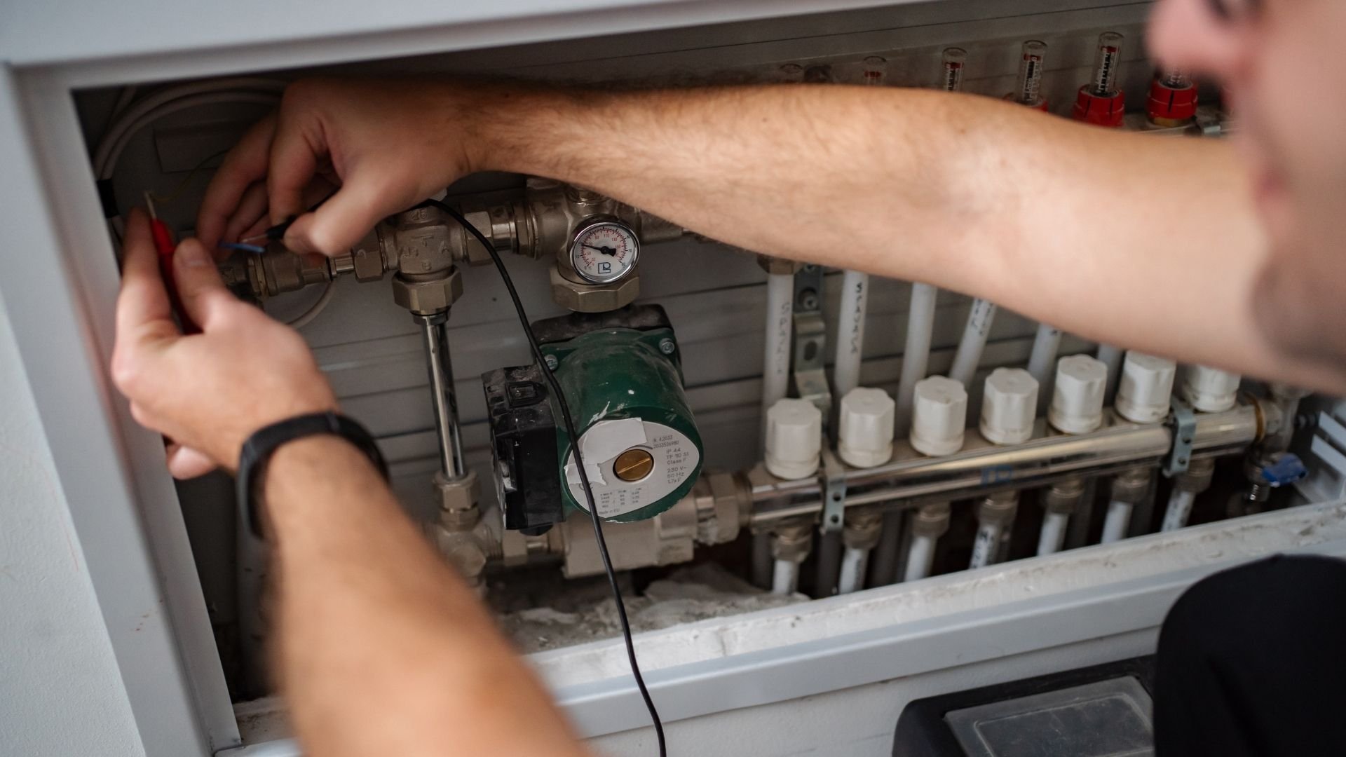 Technician inspecting heating system manifold with thermometer and multiple white valve connections