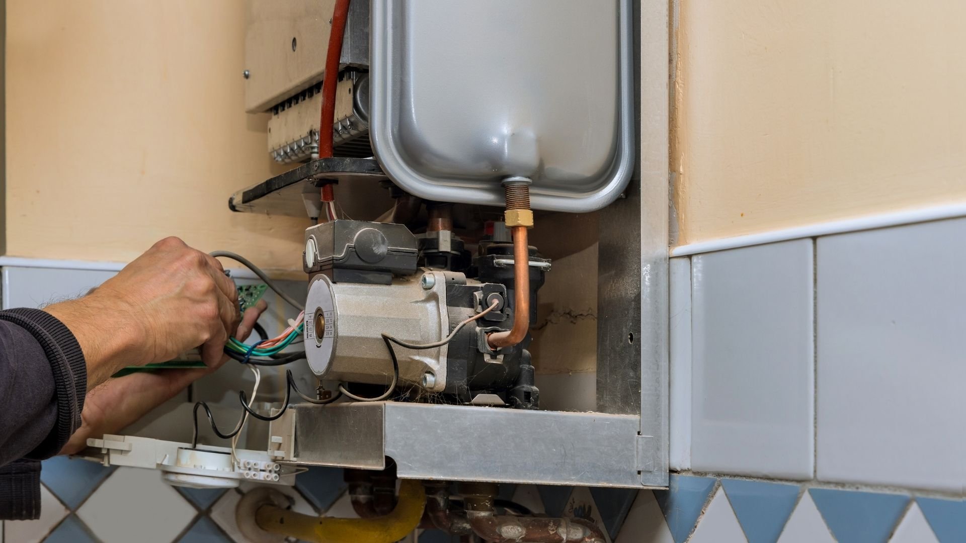 Technician repairing internal components of wall-mounted water heater unit.