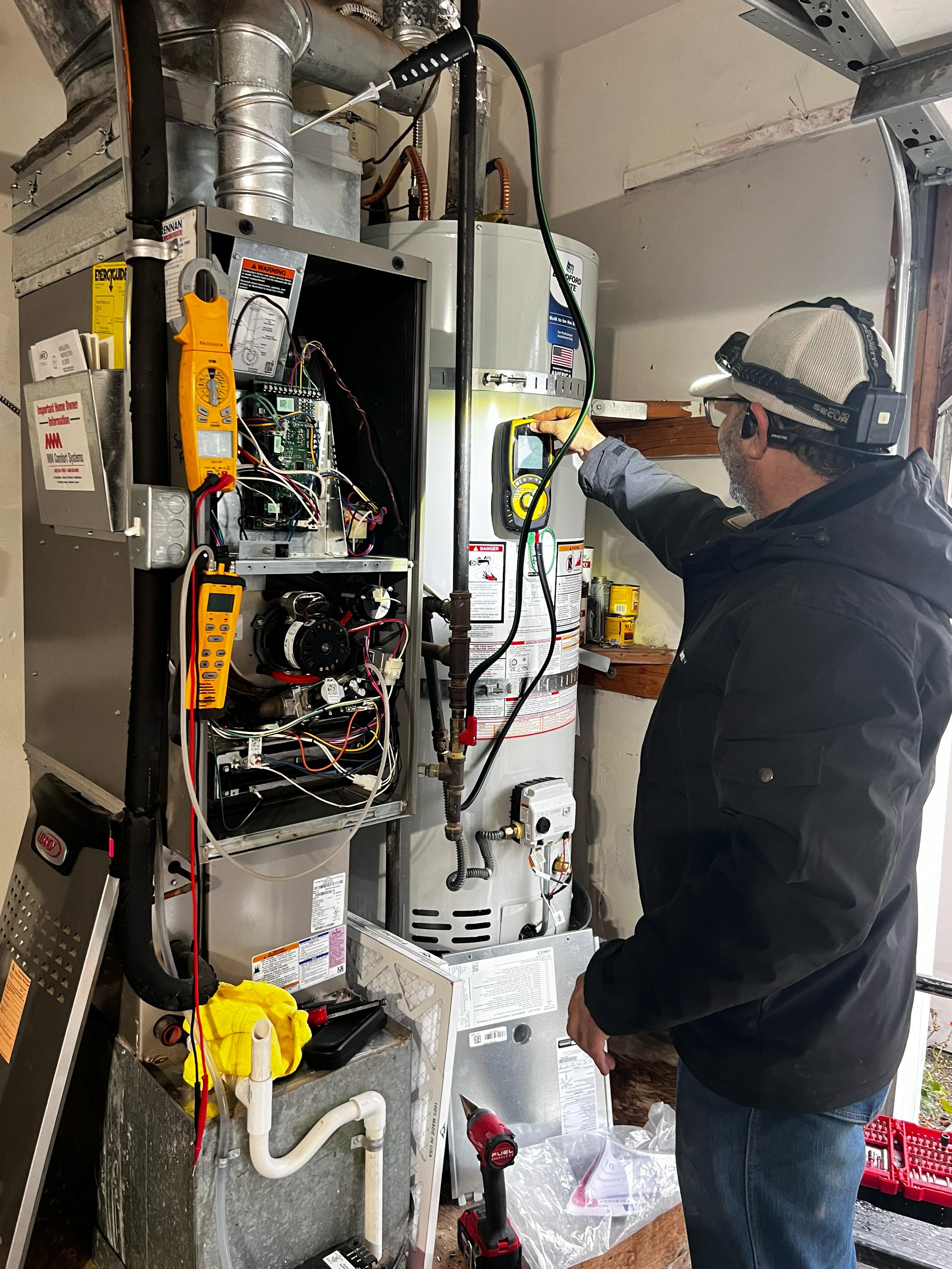 HVAC technician inspecting open furnace unit with testing equipment indoors.