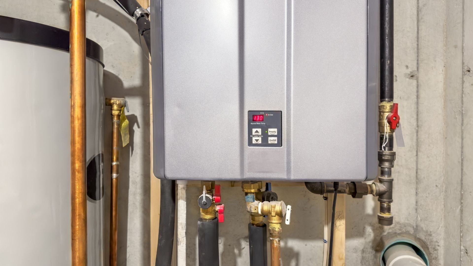 Digital tankless water heater mounted on wall with copper piping and brass valves