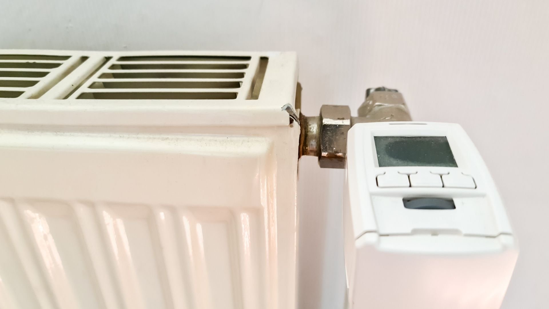 Wall-mounted white radiator with digital thermostat control panel on beige wall.